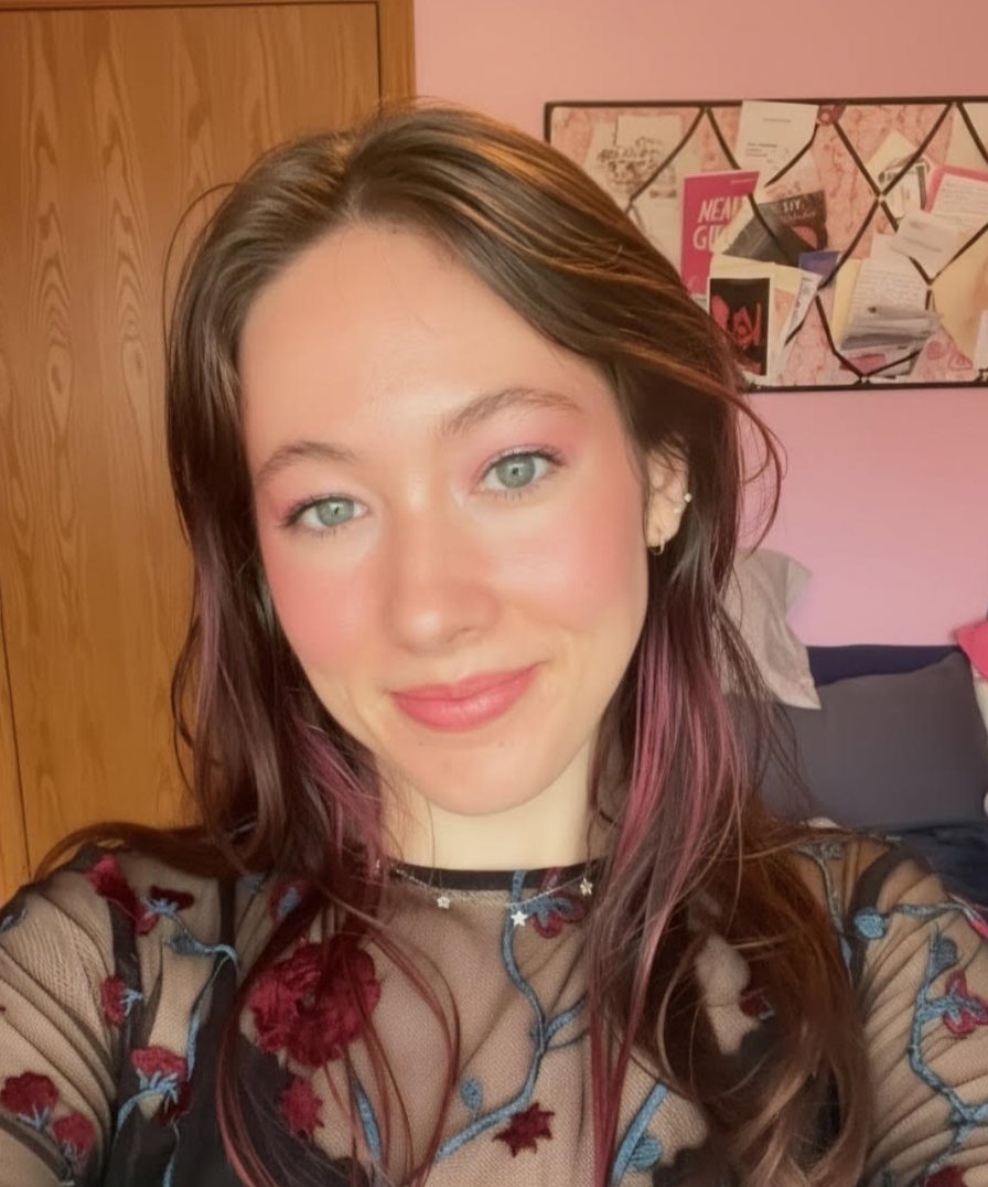 Romance author Lucy Hartfield smiling, wearing a sheer top embroidered with red roses